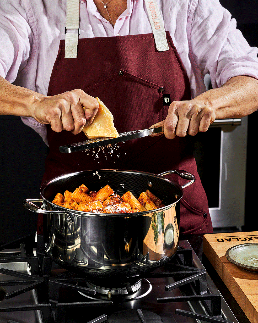 Person grating cheese over a pot of pasta on a stove.