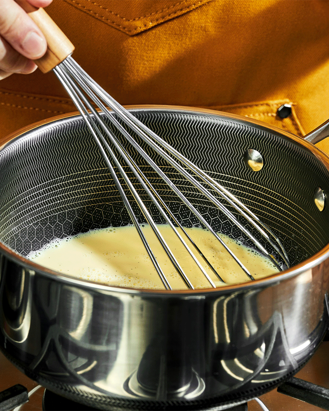 Person whisking liquid in a stainless steel pot on a stove.
