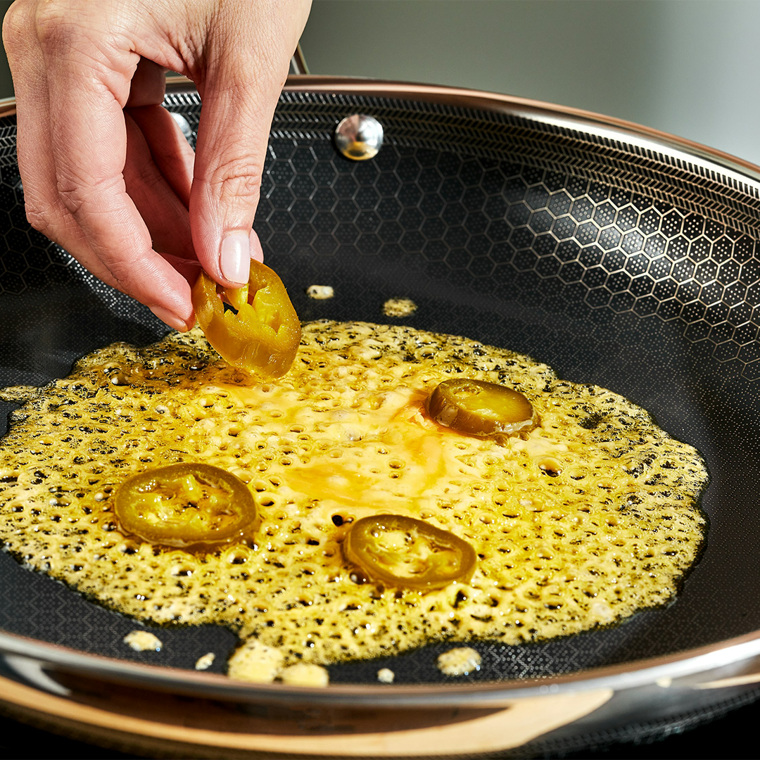 Hand placing jalapeño slices in a frying pan with bubbling oil.