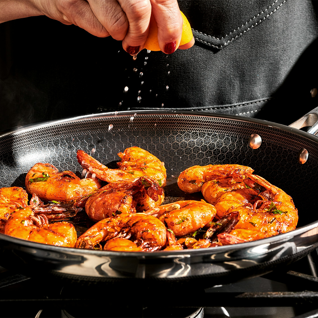 Person squeezing lemon over shrimp cooking in a pan.