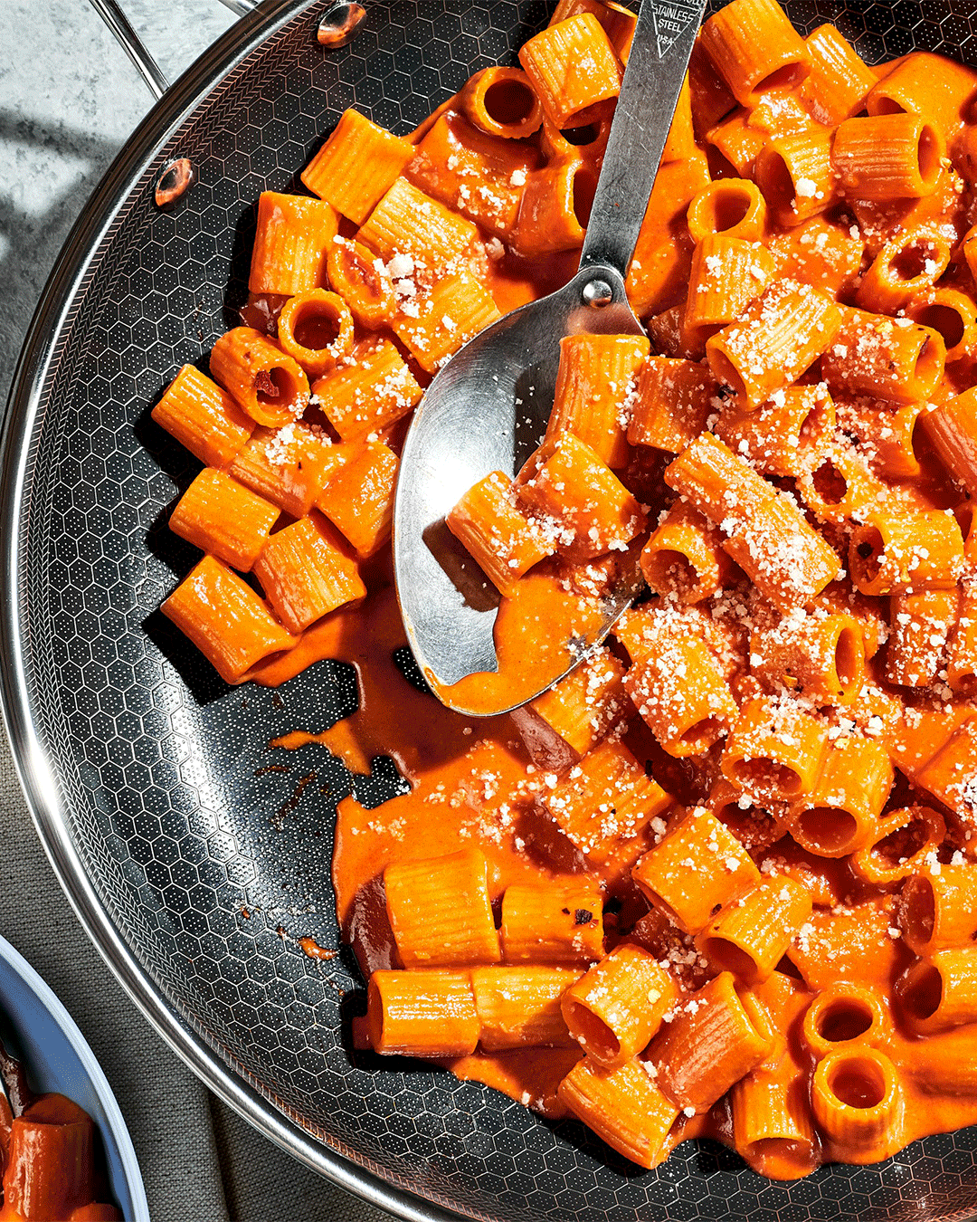Pasta with red sauce and cheese in a pan with a serving spoon.