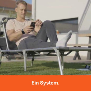 A man in white socks relaxes on a lounge chair outdoors, looking at his smartphone.