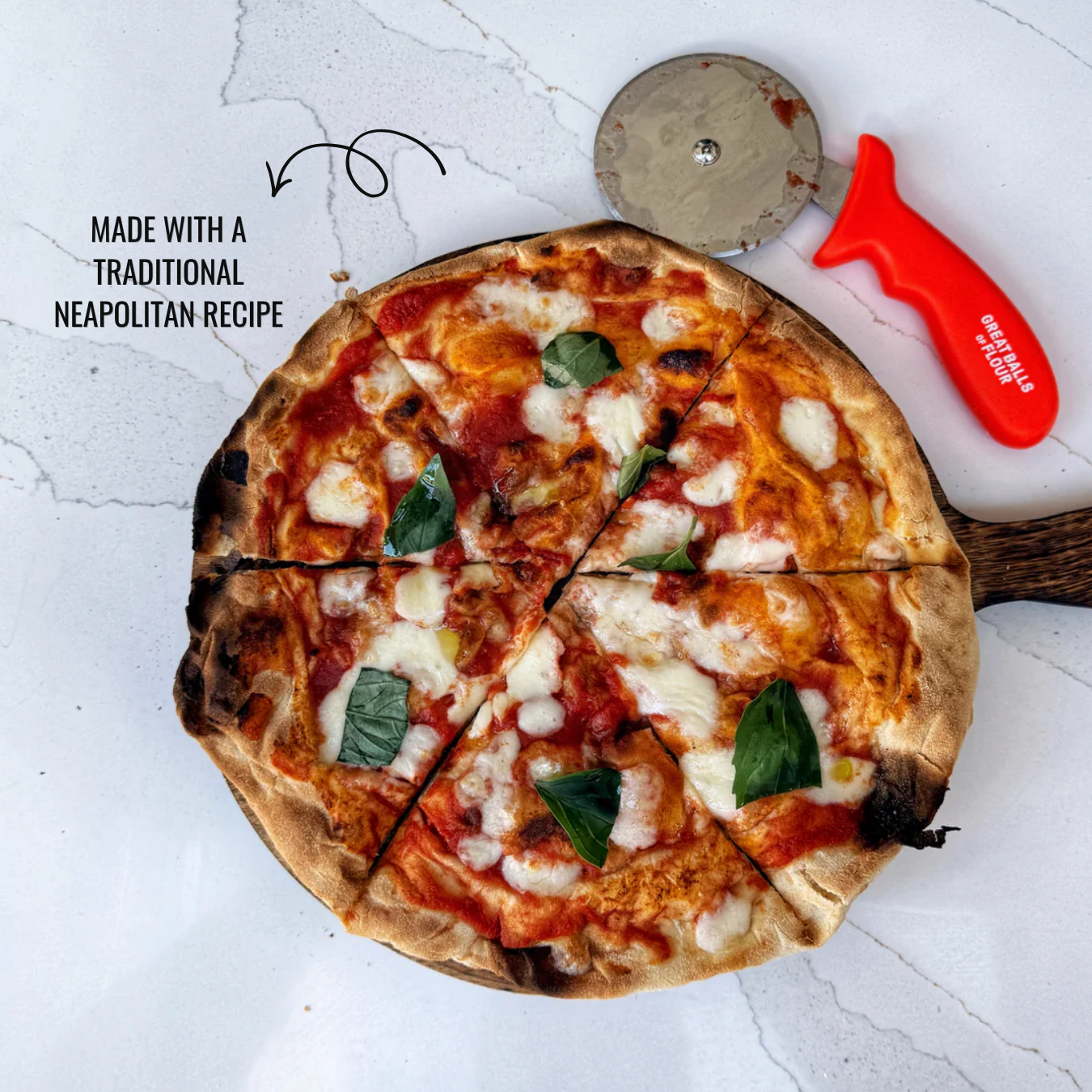 An overhead shot of a sliced Neapolitan pizza on a wooden board next to a red pizza cutter.