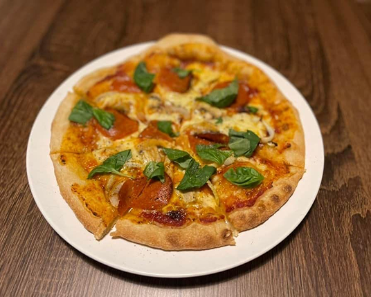 A sliced pizza topped with pepperoni and basil, served on a white plate on a wooden surface.