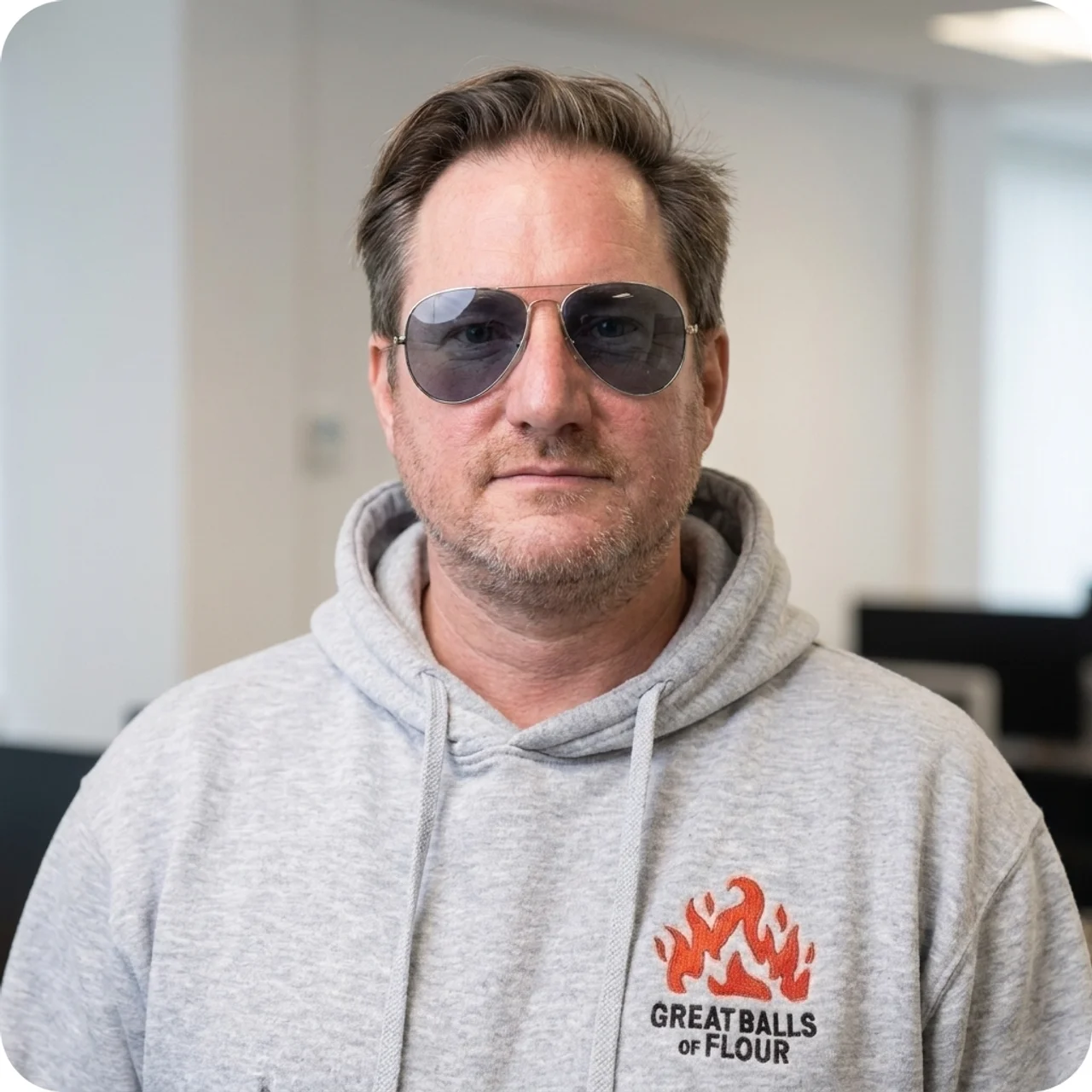 A man wearing aviator sunglasses and a grey hoodie with a 'Great Balls of Flour' logo.