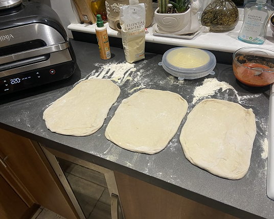Three portions of raw, flattened dough on a floured kitchen worktop, ready for cooking.