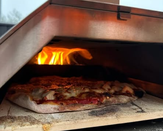 A close-up of a pizza with melted cheese baking on a stone inside a flaming pizza oven.