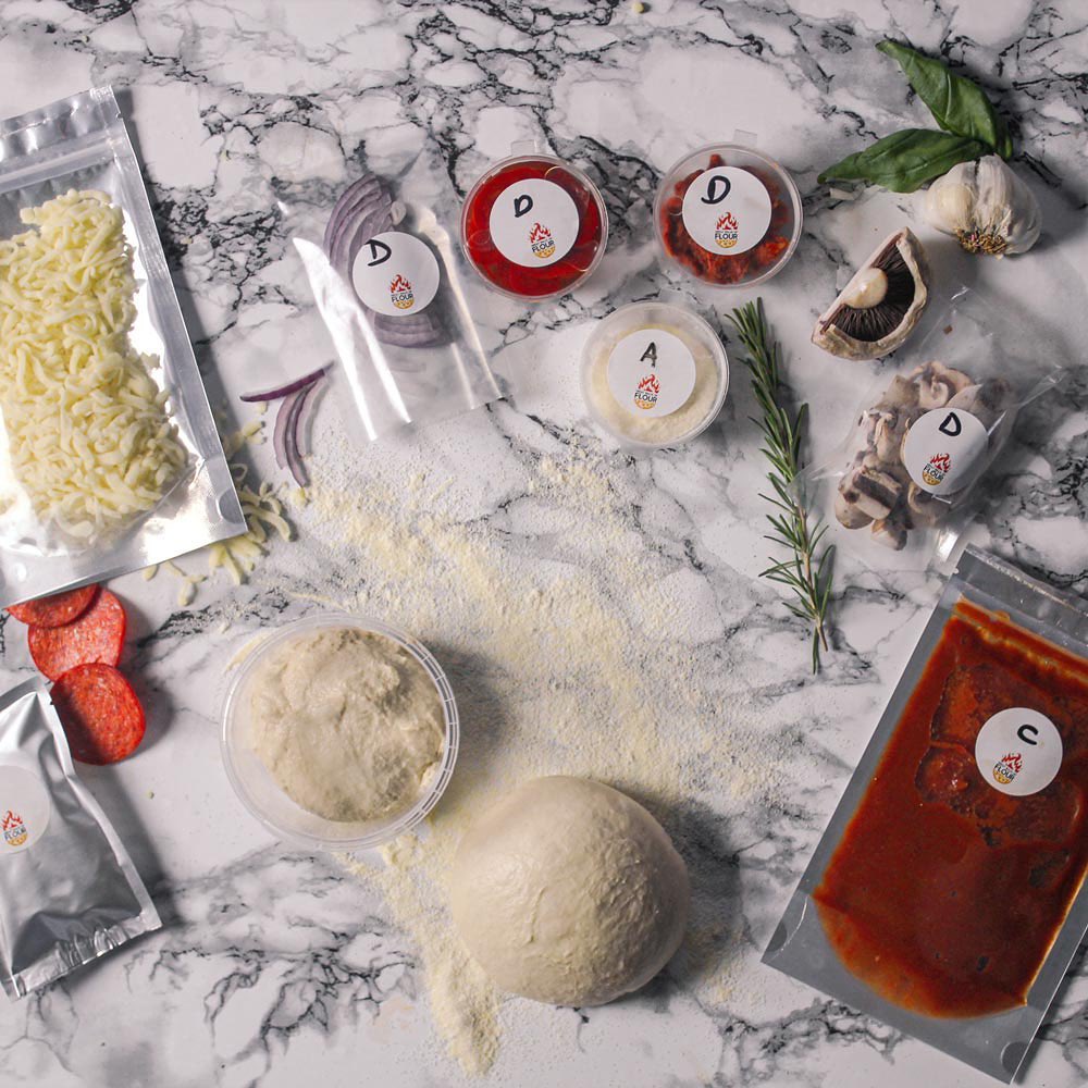 A top-down view of a pizza-making kit with various ingredients arranged on a marble countertop.