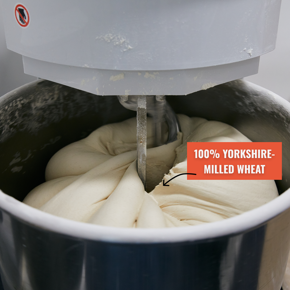 A close-up of an industrial mixer kneading a large batch of dough in a metal bowl.