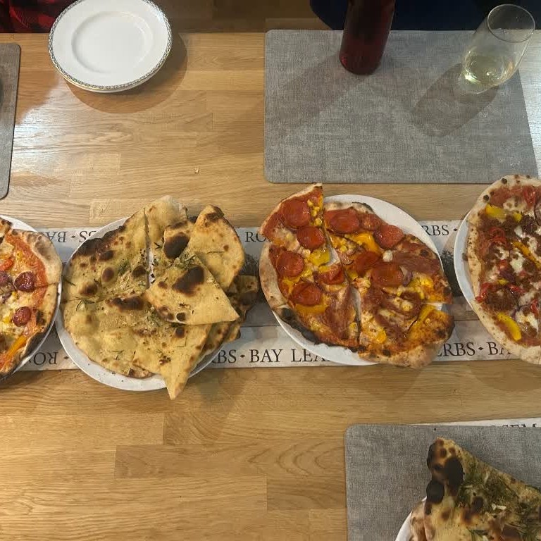 An overhead view of several pizzas and some flatbread served on a wooden table.