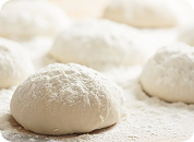 A close-up of several balls of fresh dough resting on a surface heavily dusted with flour.