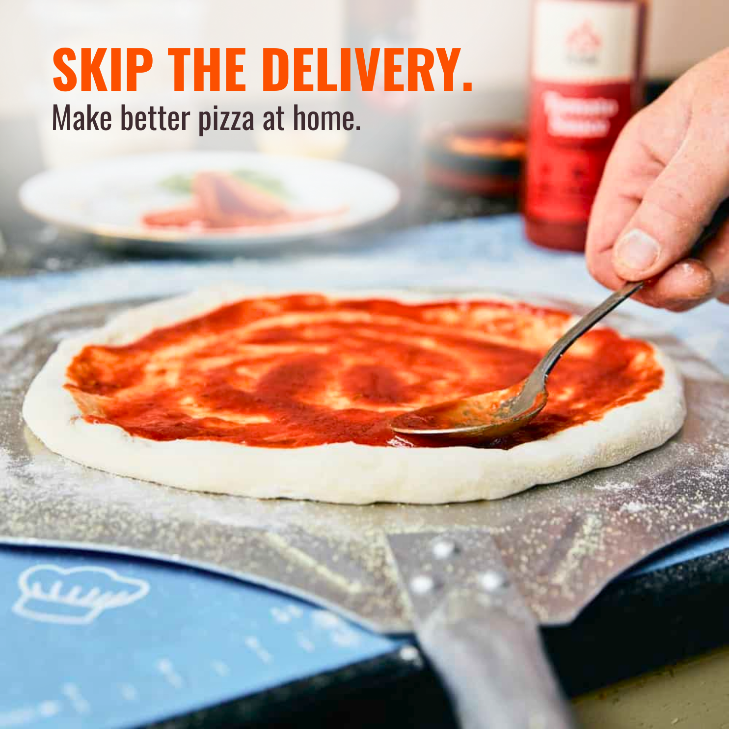 A person spreads tomato sauce on a raw pizza dough with a spoon on a pizza peel.