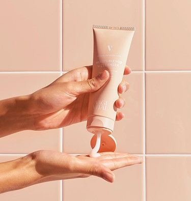 Hands applying cleanser from a squeeze tube against a tiled background.