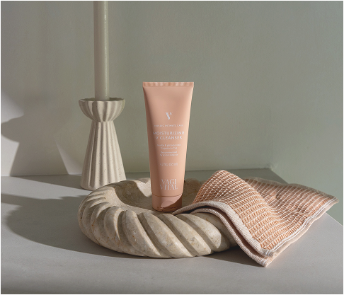 Skincare cleanser tube on decorative tray with textured cloth, beside a candle.