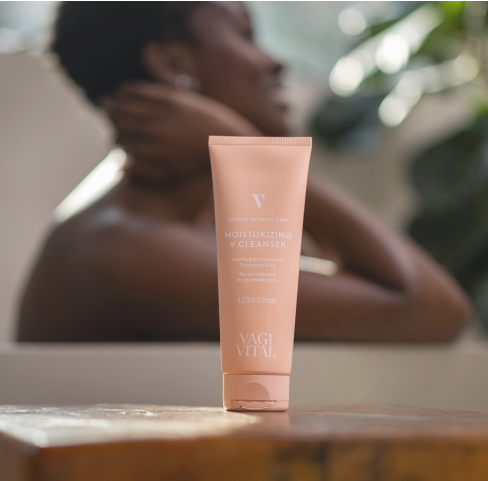 A tube of moisturizing cleanser on a surface, with a person blurred in the background.