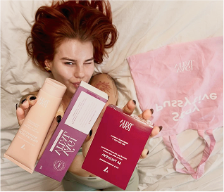 Person holding beauty products with pink bag in the background.