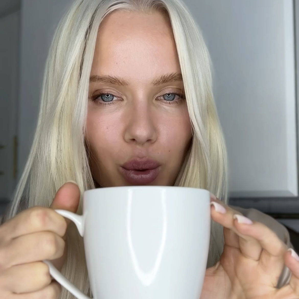 Person with long blonde hair holding a white mug.