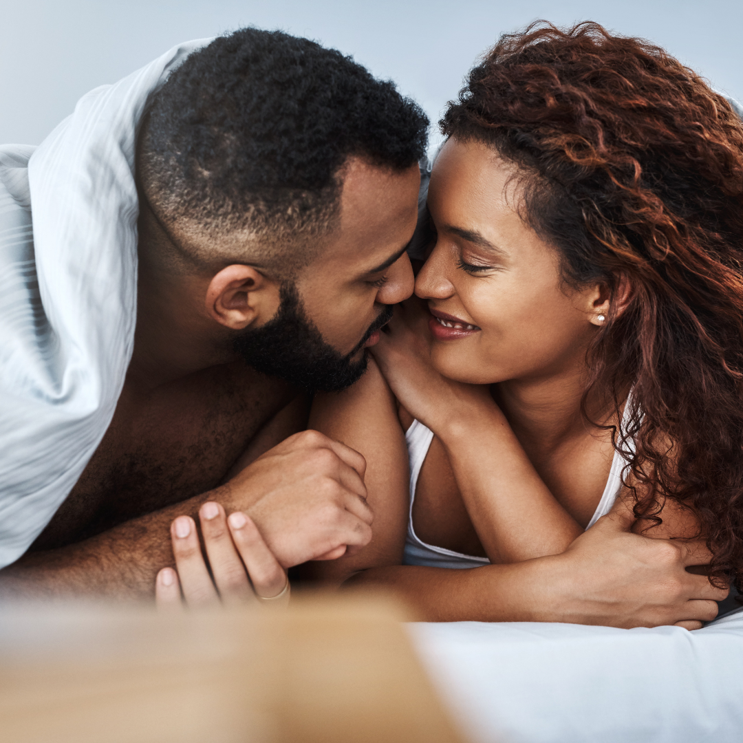 Couple lying in bed, smiling and embracing under a blanket.