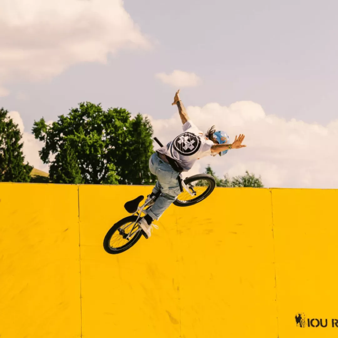 Person performing BMX trick against yellow wall and sky background.