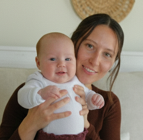 A woman with dark hair holds a smiling baby while both look towards the camera.