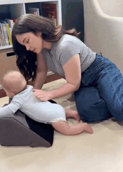 Woman playing with a baby on the floor beside a bookshelf.