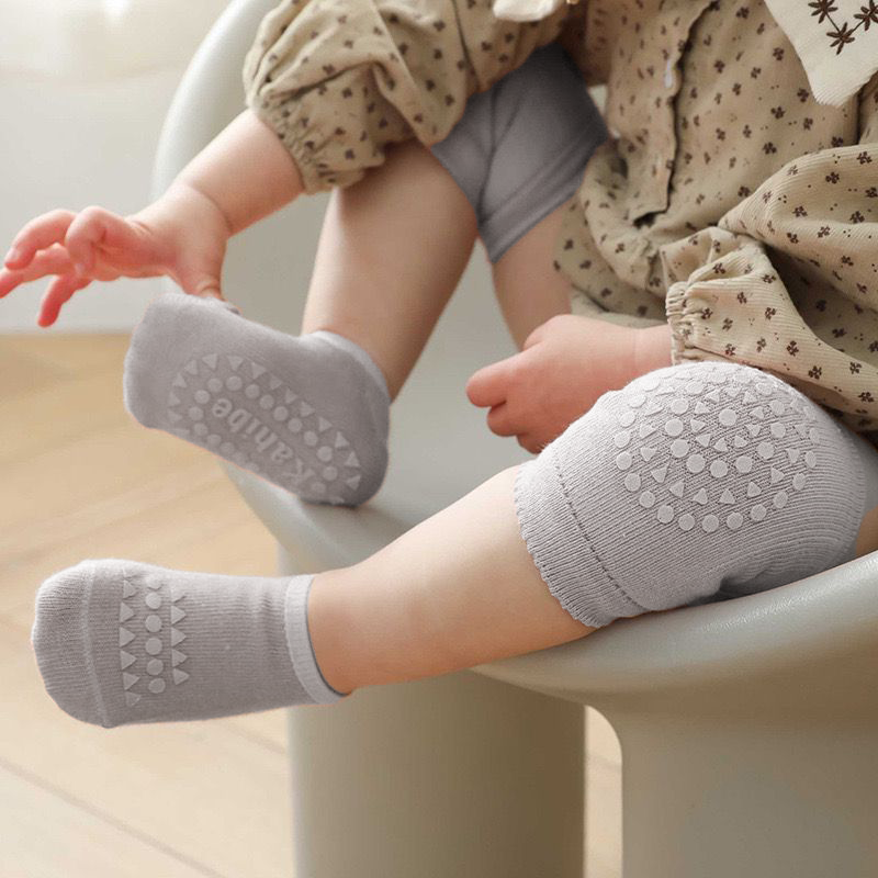 Baby wearing gray kneepads and socks, sitting on a chair.