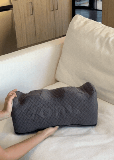 Person holding a gray quilted pillow on a white couch.