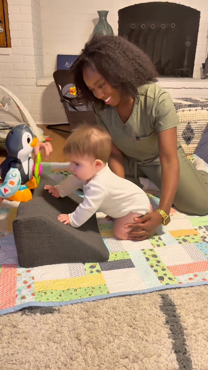 Woman helping baby play with a penguin toy on a colorful quilt.