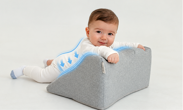 A smiling baby lies on a grey wedge-shaped pillow with blue arrows indicating spinal support.
