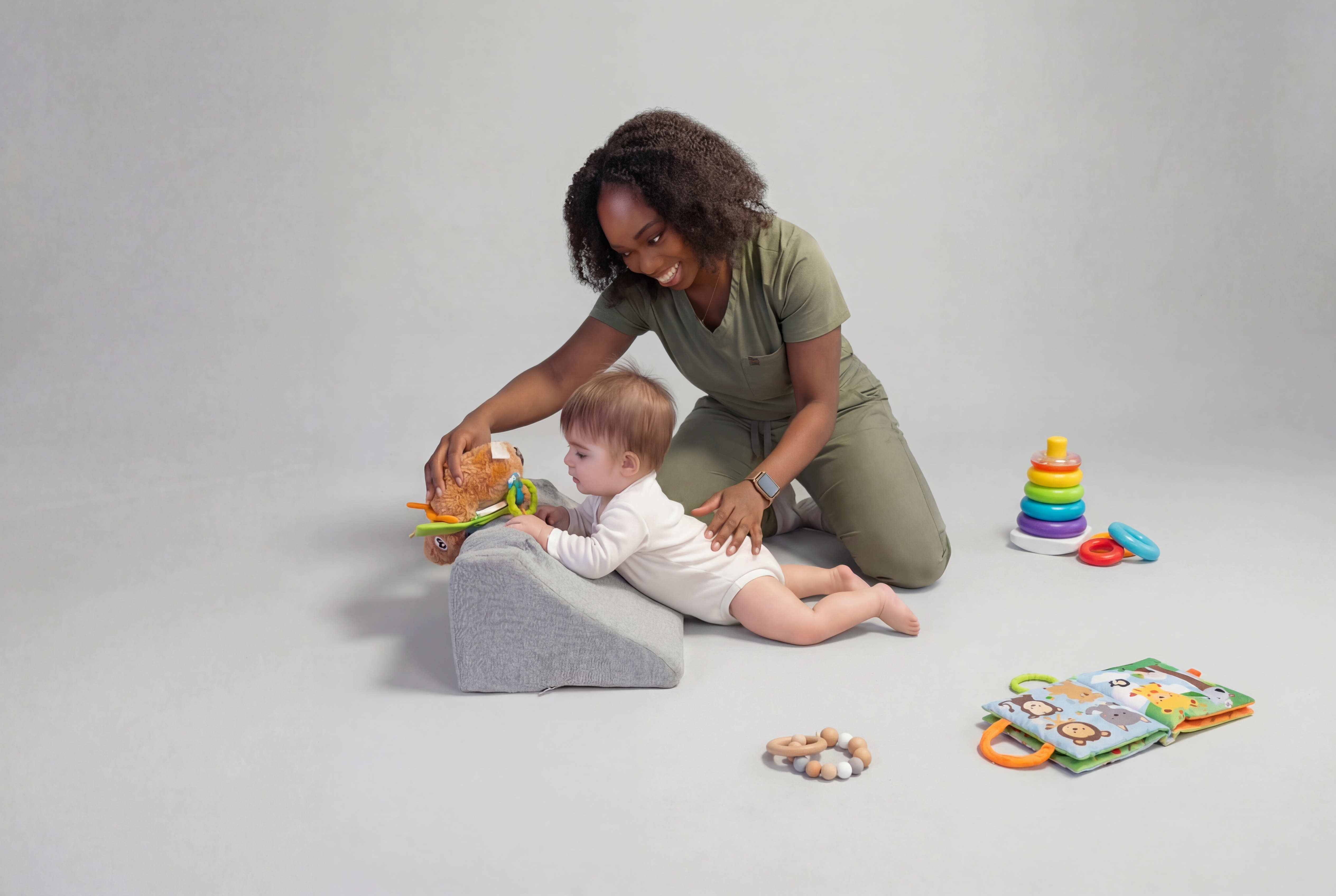 Woman playing with a baby on a cushion, with toys scattered around.