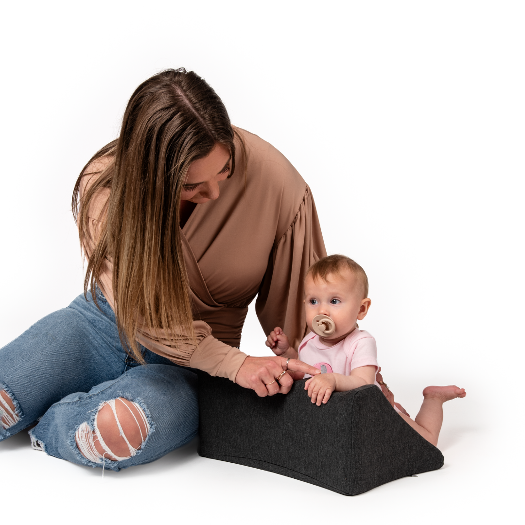 Woman sitting with a baby using a support cushion, both on a white background.