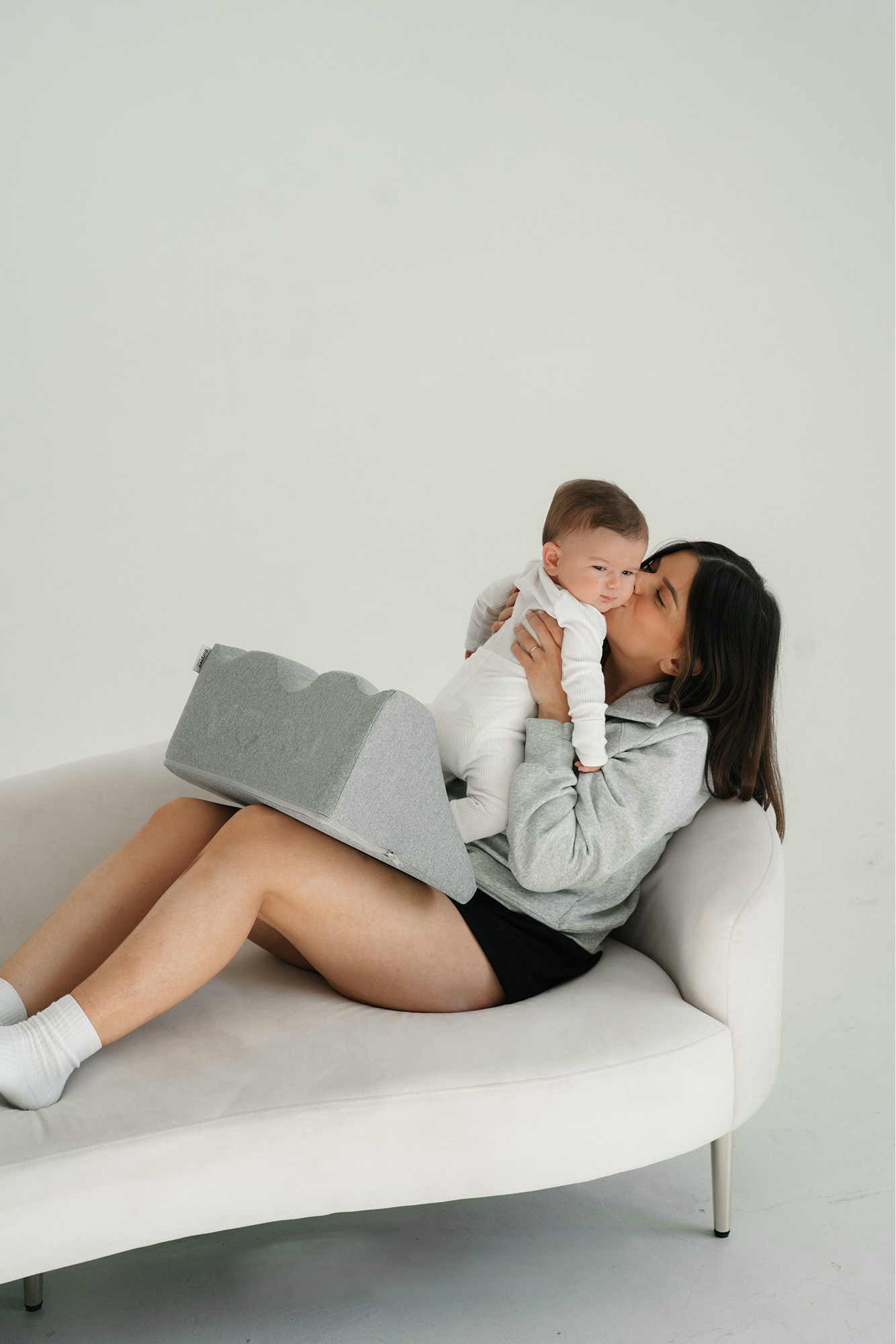 Woman sitting on a couch kissing a baby in white clothing.