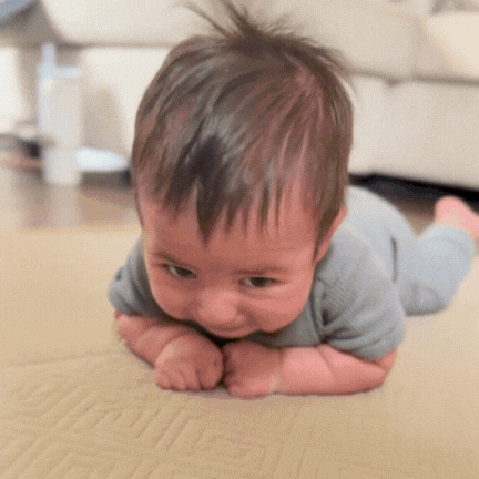 Baby lying on stomach, looking down, in a gray outfit on a mat.