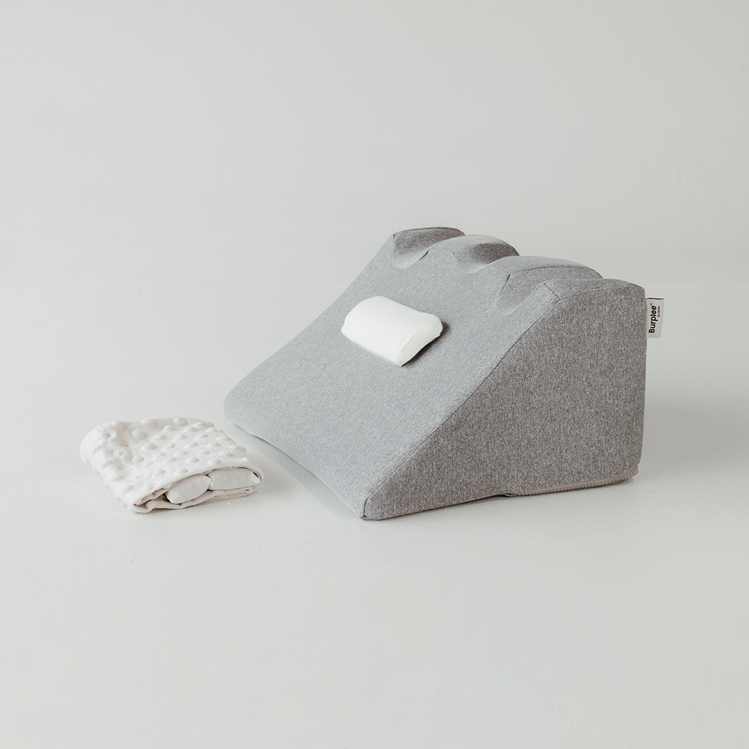 Gray wedge pillow and white textured cloth on a white surface.