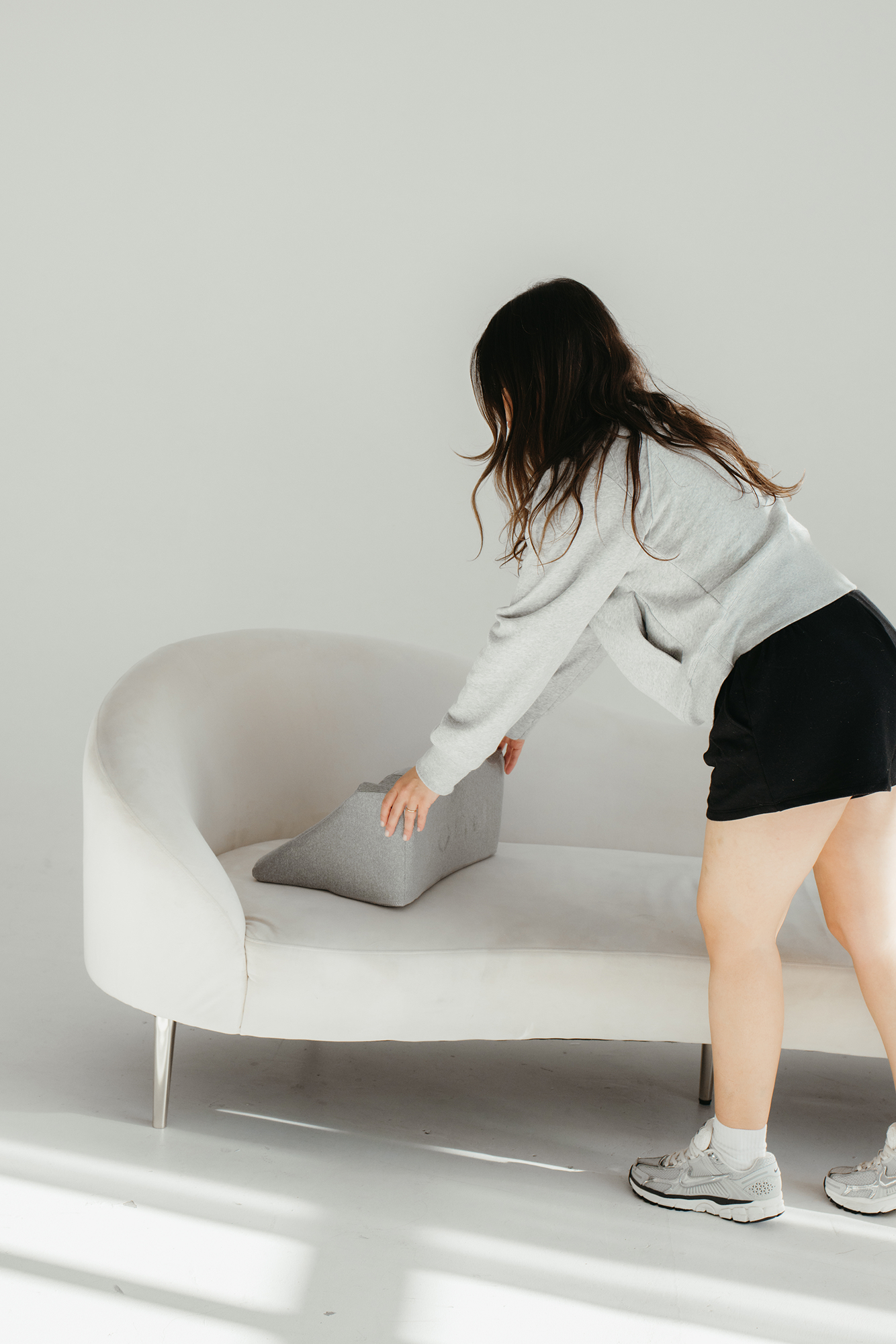 Person arranging pillow on a white couch.
