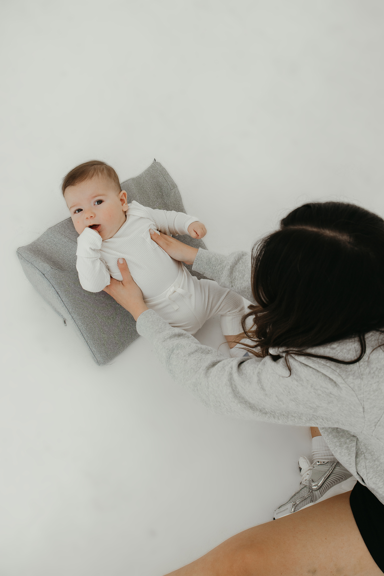 Baby lying on a cushion with a woman in a gray sweatshirt.