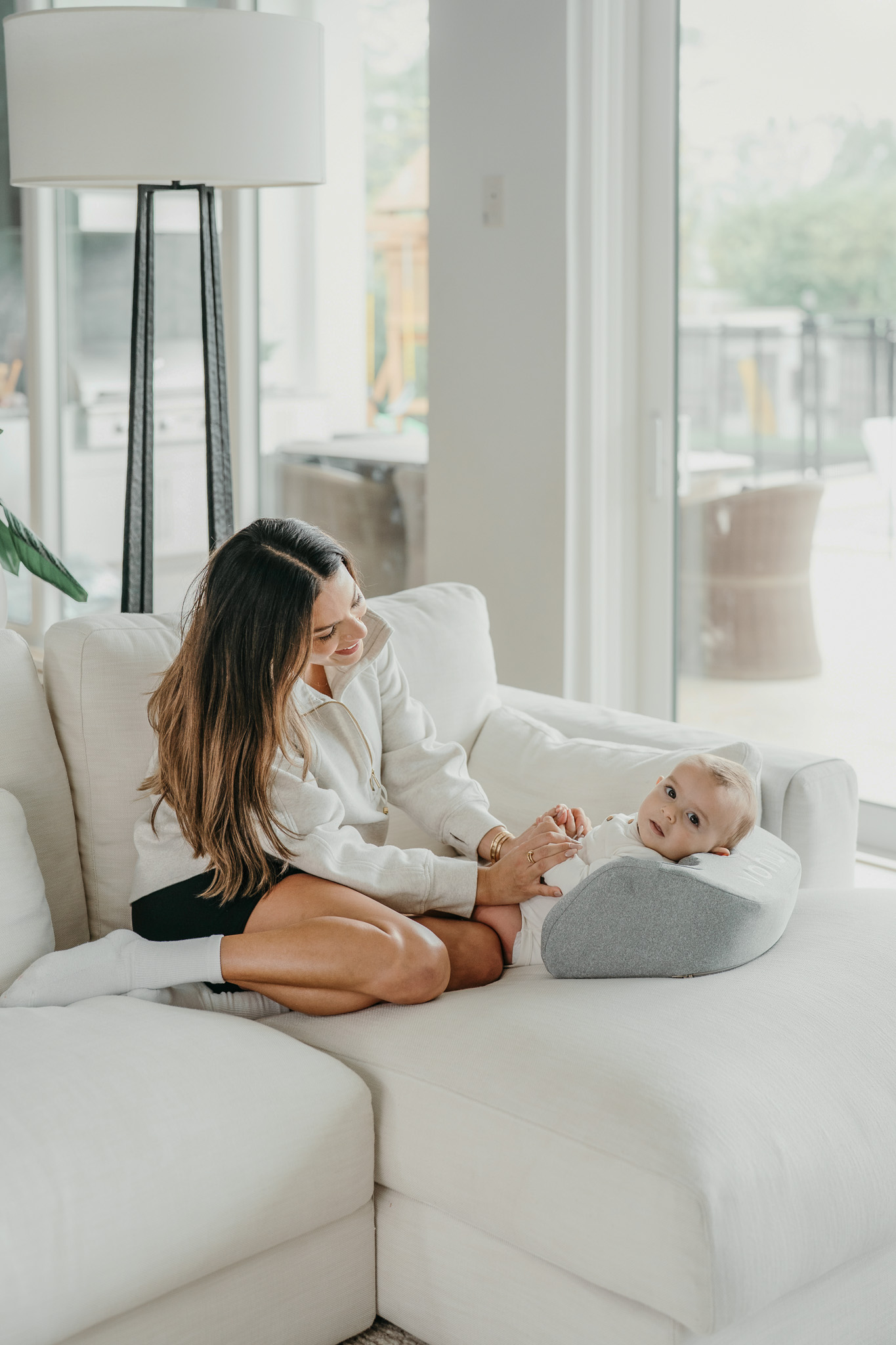 Woman sitting on a couch smiling at a baby in a gray pillow.