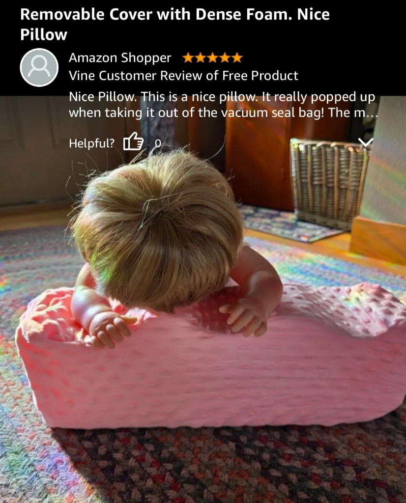 A screenshot of an Amazon review showing a baby doll lying face down on a pink pillow.