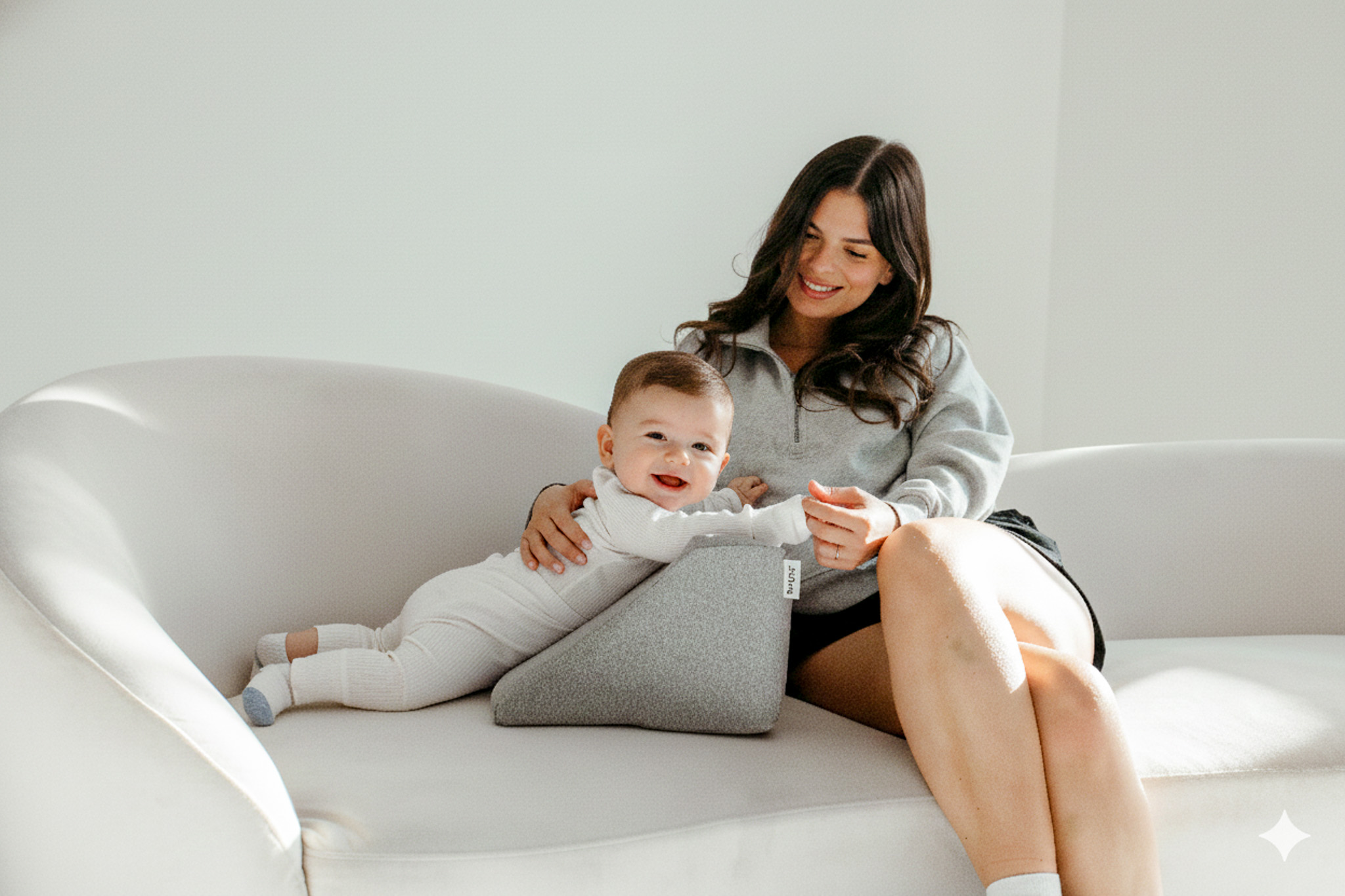 Woman sitting with a baby leaning on a gray cushion.