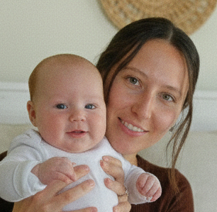 A smiling woman with dark hair holds a baby who is looking at the camera.