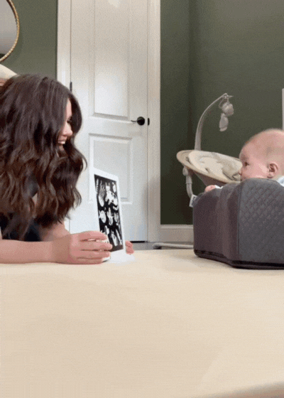 Woman showing a picture to a baby seated in a cushion chair.