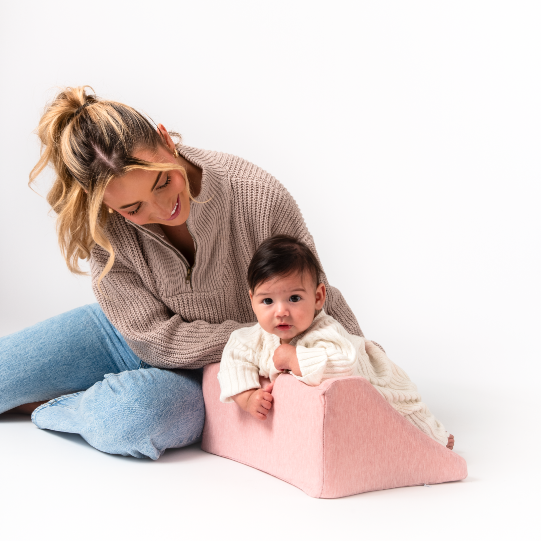 Woman sitting with a baby on a pink cushion, both smiling.
