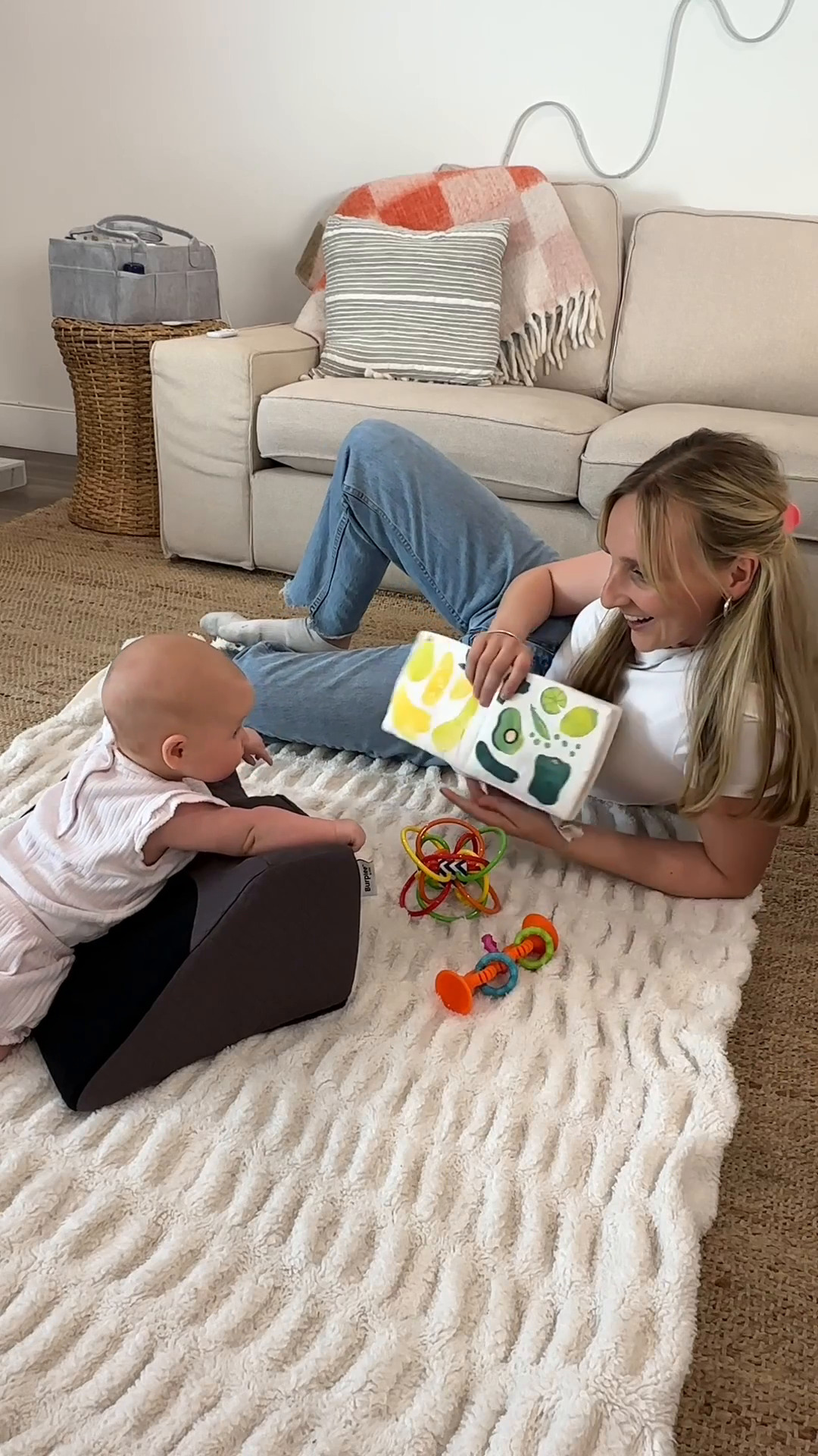 Woman reading a book to a baby on a play mat.