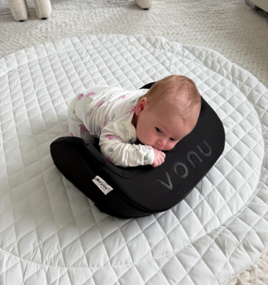 Baby lying on a black cushion on a quilted mat.