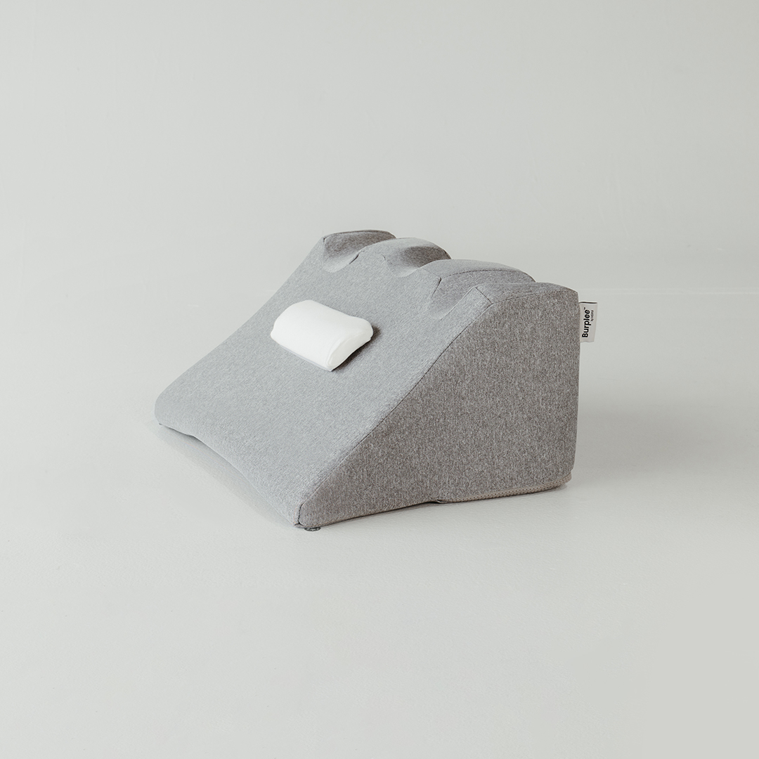 Gray cushion with a small white pillow attached, on a plain background.