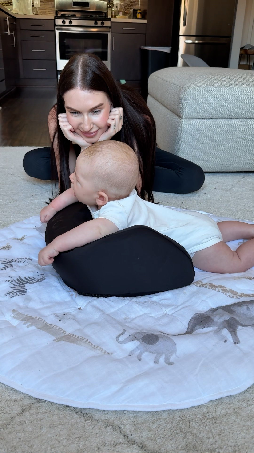 Person smiling at a baby on a cushion in a kitchen setting.