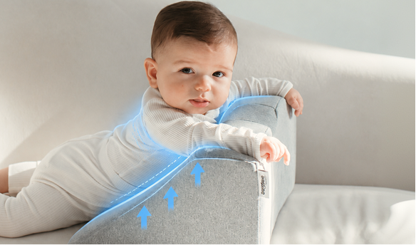 A baby lies on a grey wedge pillow with blue graphics indicating support on a white couch.
