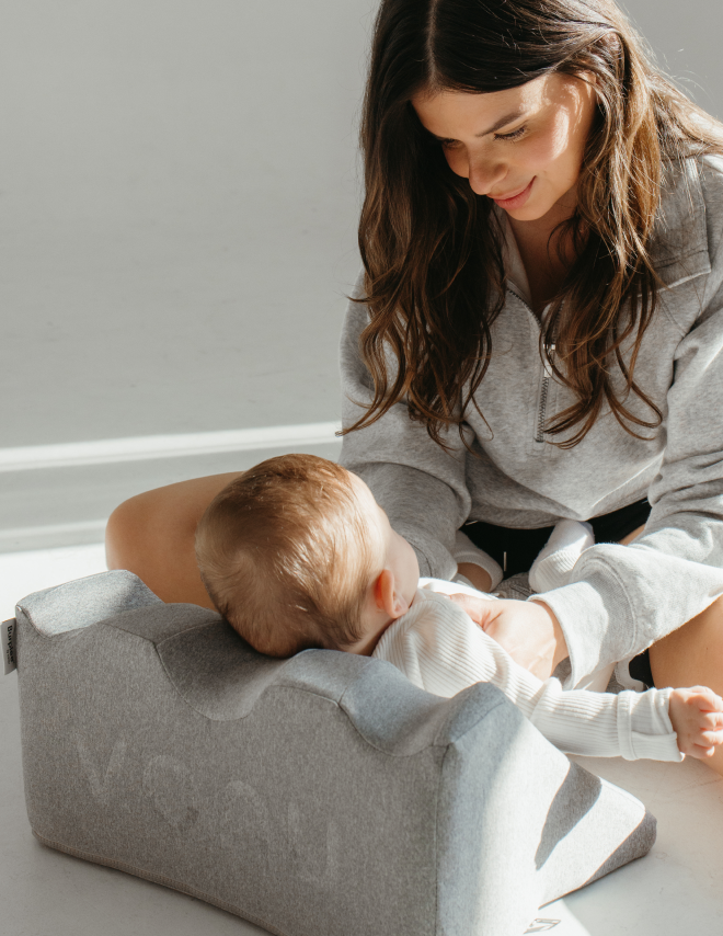 Woman smiling at a baby on a pillow.