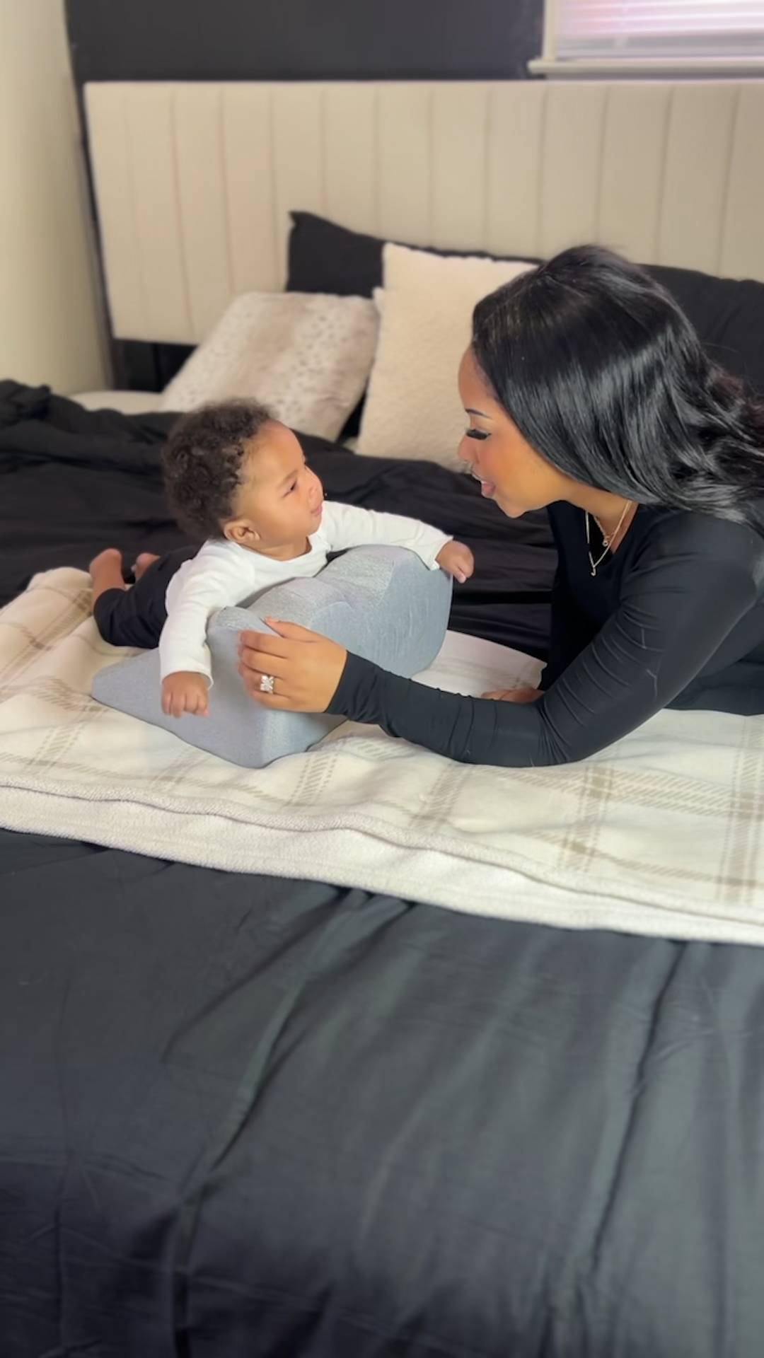 Woman and baby interacting on a bed with a pillow.