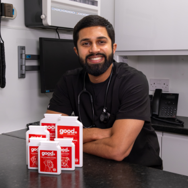 A smiling veterinarian stands behind a desk with several bottles of 'good.' brand pet supplements.